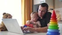 Otac drži dete i radi na laptopu