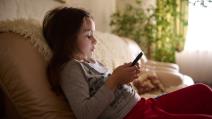 Devojčica sedi na kauču držeći telefon