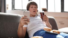 Tinejdžer sedi na krevetu, jede i pije i gleda u telefon