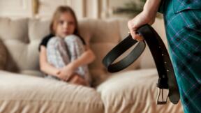 Mama drži kaiš ispred devojčice koja sedi sklupčana na kauču