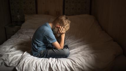 Tužan dečak sedi na krevetu