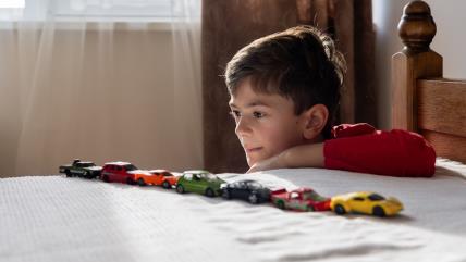 Dečak sa poređanim autićima na krevetu