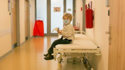 Dete sedi na krevetu u bolničkom hodniku