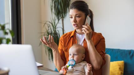 Mama drži bebu u krilu, telefonira i gleda u kompjuter