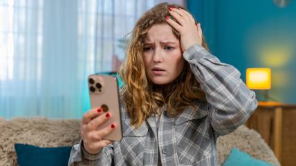 Žena sa iznenađenim izrazom lica gleda u telefon