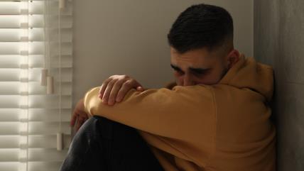 Tužan muškarac sedi na podu pored prozora