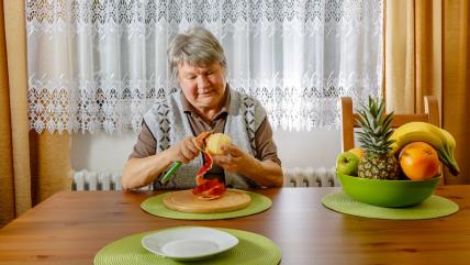 Starija žena za stolom ljušti jabuku