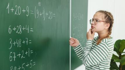 Devojčica pred školskom tablom radi matematički zadatak