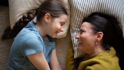 Mama i ćerka sa osmehom razgovaraju u krevetu