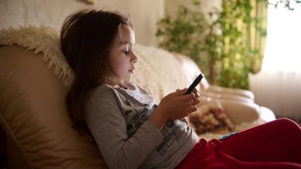 Devojčica sedi na kauču držeći telefon