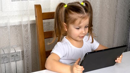 Devojčica za stolom gleda u tablet