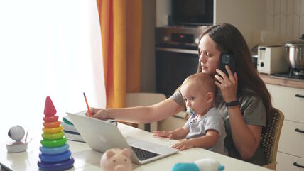 Mama sa detetom u krilu nešto zapisuje i razgovara na telefon