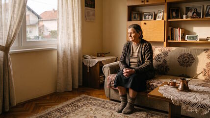 Starija žena sedi sama na kauču u dnevnoj sobi
