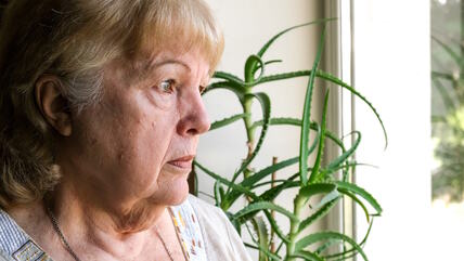 Usamljena starija žena gleda kroz prozor