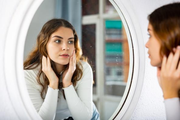 Mlada žena gleda svoje lice u ogledalu