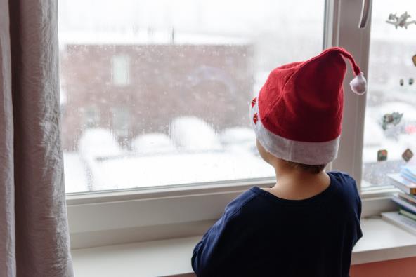 Dečak sa kapicom Deda Mraza gleda kroz prozor