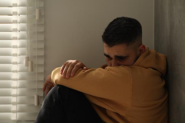 Tužan muškarac sedi na podu pored prozora