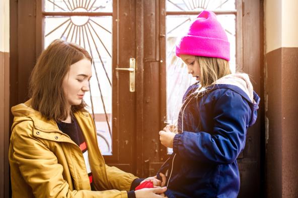 Mama zakopčava jaknu devojčici