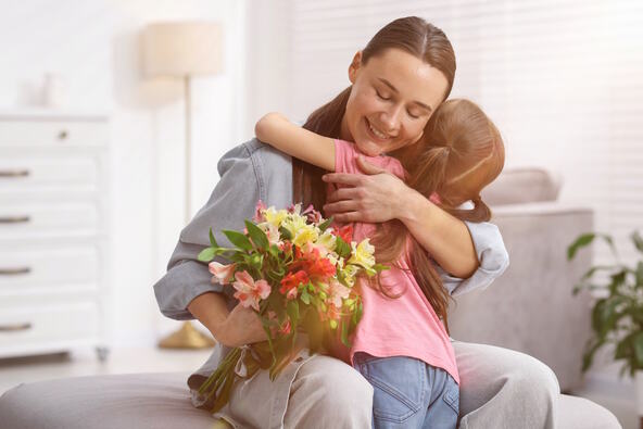 Devojčica daje mami buket cveća i grli je