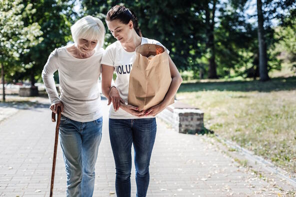 Starija žena hoda sa štapom i oslanja se na mlađu ženu